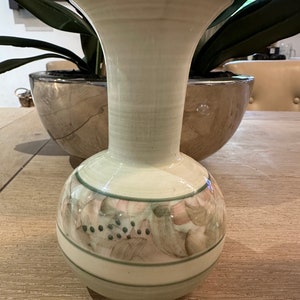 May include: A ceramic vase with a wide mouth and a round body. The vase is decorated with a green, brown, and white floral pattern.