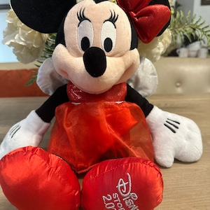 K&ouml;nnte beinhalten: Minnie Mouse Pl&uuml;schtier mit roter Schleife, Kleid und Schuhen. Das schwarz-wei&szlig;e Pl&uuml;schtier hat wei&szlig;e Handschuhe und schwarze Ohren. Das Logo Disney Store 2012 ist auf einem der roten Schuhe gestickt.