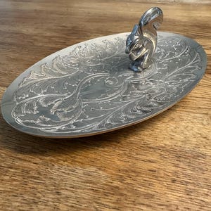 May include: A silver oval serving tray with an ornate floral design and a squirrel figurine handle.
