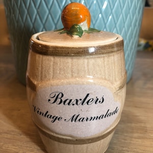 May include: A ceramic jar with a lid shaped like an orange. The jar is decorated with a brown and white striped pattern and the words "Baxter's Vintage Marmalade".