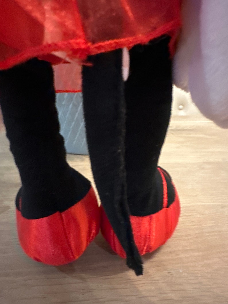 K&ouml;nnte beinhalten: Ein Pl&uuml;schtier mit schwarzen Beinen und roten Schuhen. Das Spielzeug hat einen roten Rock und ein wei&szlig;es, flauschiges Element. Die Schuhe sind leuchtend rot und die Beine sind schwarz.