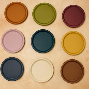 May include: Nine colorful, round coasters in shades of orange, green, burgundy, pink, teal, yellow, navy, cream, and brown. The coasters are arranged in a 3x3 grid, each with a slightly raised edge.