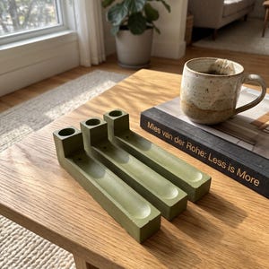 May include: Three olive green rectangular incense holders made of a solid material, each featuring a cylindrical opening at one end and a long, narrow, concave channel running along the top surface for holding incense sticks.