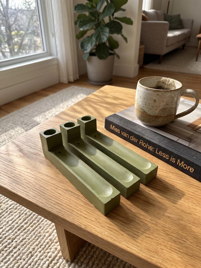 May include: Three olive green rectangular incense holders made of a solid material, each featuring a cylindrical opening at one end and a long, narrow, concave channel running along the top surface for holding incense sticks.