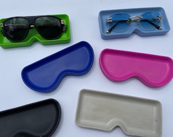 Peut inclure: Cinq plateaux en plastique de couleurs différentes conçus pour contenir des lunettes de soleil. Les plateaux sont en forme de lunettes de soleil et sont de couleur bleue, rose, verte, noire et grise.