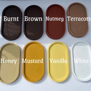 May include: Eight oval-shaped trays arranged in two rows, featuring colours labelled as Burnt, Brown, Nutmeg, Terracotta, Honey, Mustard, Vanilla, and White. Each tray has a smooth, solid-coloured surface with a raised rim, presented in a grid layout.