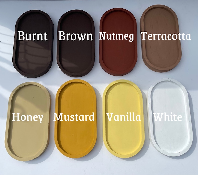 May include: Eight oval-shaped trays arranged in two rows, featuring colours labelled as Burnt, Brown, Nutmeg, Terracotta, Honey, Mustard, Vanilla, and White. Each tray has a smooth, solid-coloured surface with a raised rim, presented in a grid layout.