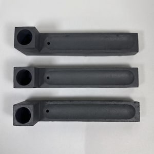 May include: Three dark grey rectangular incense holders arranged horizontally. Each piece features a square block on the left side with a circular opening and a long, narrow, recessed channel extending to the right, ending with a small hole.