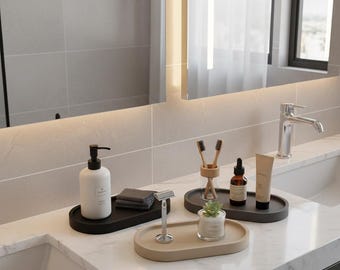 Peut inclure: Accessoires de salle de bain disposés sur un comptoir en marbre. Comprend un distributeur de savon noir, des débarbouillettes grises, un rasoir et des plateaux ovales contenant des articles de toilette, des brosses à dents et une petite plante.