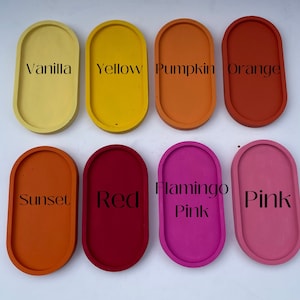 May include: Eight oval-shaped trays arranged in two rows, labelled with text: Vanilla, Yellow, Pumpkin, Orange, Sunset, Red, Flamingo Pink, and Pink. Each tray features a solid, matte-finish colour corresponding to its label, showcasing a smooth surface.