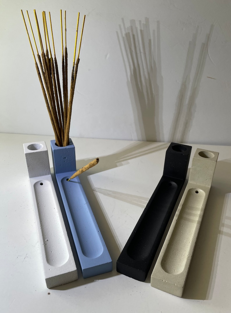 May include: Four L-shaped incense holders in white, light blue, black, and beige. Each holder features a rectangular base with a long, shallow groove and a vertical block at one end containing a circular opening for incense sticks.