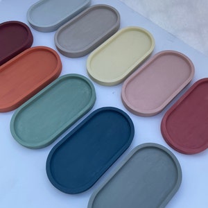 May include: Ten oval-shaped concrete trays in various colors, including light blue, green, beige, yellow, pink, red, and dark blue. The trays are arranged in a semi-circle on a white surface.