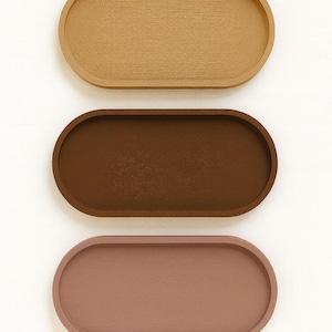 May include: Three oval-shaped trays in a vertical arrangement. The top tray is a light tan color, the middle tray is a dark brown, and the bottom tray is a muted rose color. The trays have a smooth, matte finish.
