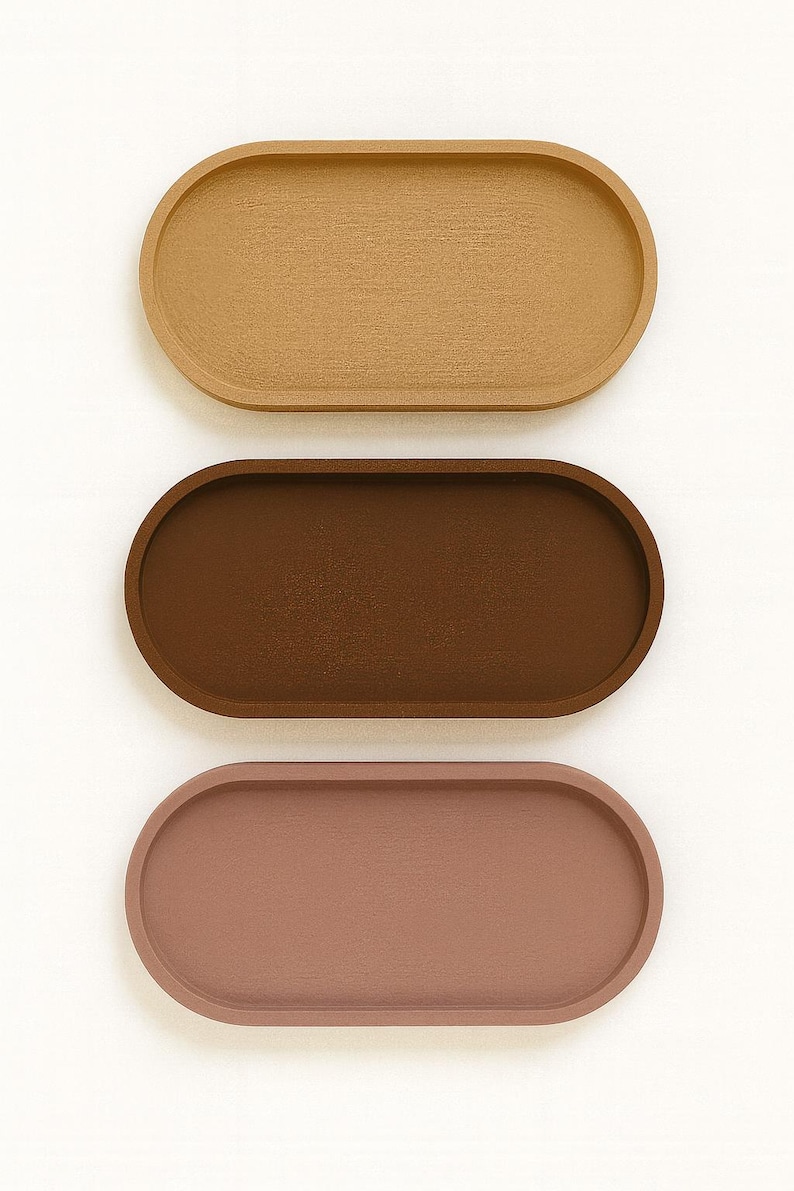 May include: Three oval-shaped trays in a vertical arrangement. The top tray is a light tan color, the middle tray is a dark brown, and the bottom tray is a muted rose color. The trays have a smooth, matte finish.
