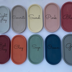 May include: Ten oval-shaped trays arranged in two rows, featuring colours labelled Light Grey, Concrete, Sand, Pink, Blush, Red Clay, Clay, Sage, Ocean, and Grey. Each tray has a smooth, solid-coloured surface with a raised rim and a matte finish.
