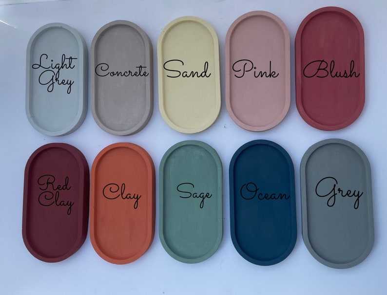 May include: Ten oval-shaped trays arranged in two rows, featuring colours labelled Light Grey, Concrete, Sand, Pink, Blush, Red Clay, Clay, Sage, Ocean, and Grey. Each tray has a smooth, solid-coloured surface with a raised rim and a matte finish.