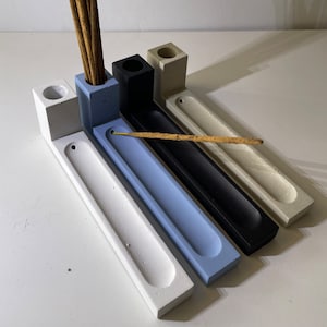 May include: Four rectangular incense holders made of concrete in white, light blue, black, and beige. Each holder features a vertical block with a circular hole for upright incense sticks and a long, narrow horizontal tray for horizontal sticks.