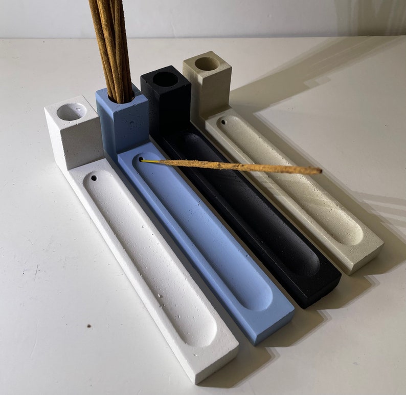 May include: Four rectangular incense holders made of concrete in white, light blue, black, and beige. Each holder features a vertical block with a circular hole for upright incense sticks and a long, narrow horizontal tray for horizontal sticks.