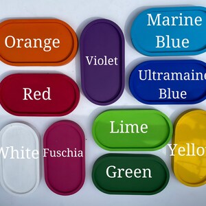 May include: A collection of eleven oval trays in various solid colours including orange, violet, marine blue, red, ultramarine blue, white, fuschia, lime, green, and yellow, each labelled with its corresponding colour name in white text.