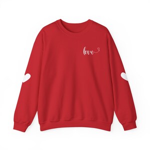 May include: A red sweatshirt with the word "love" in white script on the chest and a white heart on each sleeve. The sweatshirt is a crew neck style.