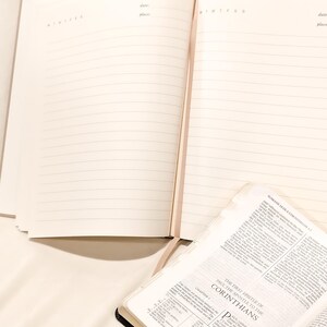 Pu&ograve; includere: Un diario beige aperto con pagine a righe, accanto a una Bibbia aperta. Il diario ha intestazioni per data e luogo. La Bibbia &egrave; aperta al primo capitolo di Corinzi.