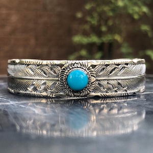 May include: A silver bracelet featuring a turquoise stone set within a feather design.
