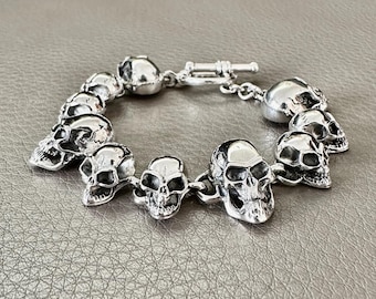 May include: A silver bracelet with a skull design. The bracelet is made up of multiple skull charms connected by a silver chain.