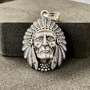 May include: Silver pendant featuring a detailed depiction of a Native American chief wearing a headdress with feathers. The pendant is a traditional design and would make a great gift for anyone interested in Native American culture.