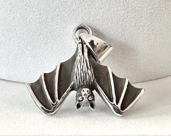 May include: A silver pendant in the shape of a bat hanging upside down. The bat has detailed wings and a textured body.