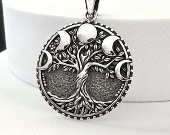 May include: A silver pendant featuring a detailed tree of life design with phases of the moon. The pendant has a circular shape with a textured background and a bail for a chain. The design is intricate and detailed.