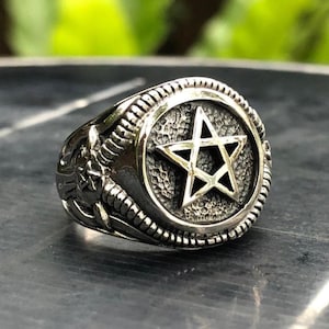 Può includere: Un anello d'argento con un design a pentagramma. L'anello ha una superficie testurizzata e un design dettagliato attorno al pentagramma.