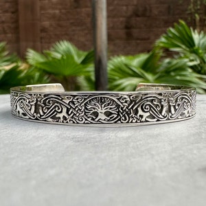 Puede incluir: Una pulsera de plata con un diseño intrincado que presenta un árbol de la vida, nudos celtas y figuras de animales estilizadas.