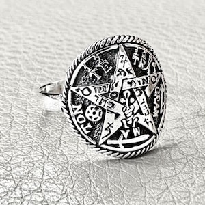 Pode incluir: Anel prateado com um design detalhado de pentagrama. O anel apresenta texto hebraico e símbolos em torno da estrela. A banda tem um padrão texturizado e o anel tem um acabamento polido. Joia.