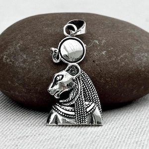 May include: A silver pendant featuring the bust of a lioness with intricate details. The pendant includes a circular element above the lioness's head and a loop for a chain. The design is set against a neutral background.