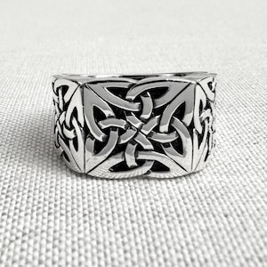Puede incluir: Un anillo plateado con un diseño de nudo celta. El anillo presenta un intrincado patrón de líneas entrelazadas, creando un diseño geométrico y simétrico. El anillo es probablemente de metal y tiene un acabado pulido.