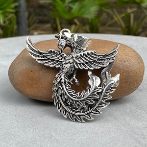 May include: A silver pendant featuring a detailed, three-dimensional phoenix design. The phoenix is depicted with outstretched wings and a long, flowing tail.
