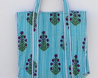 May include: A blue and white striped tote bag with a floral pattern. The bag features vertical stripes and a repeating pattern of purple flowers with green leaves. The handles are also striped.