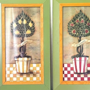 May include: Two framed rectangular wall art prints featuring stylized potted trees. The left print shows a lemon tree with the text 'l'citron' in a striped pot on a checkered surface. The right print shows a cherry tree with the text 'l'ceresia' in a striped pot on a checkered surface. Both have green and light wood frames.
