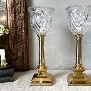 May include: A pair of gold table lamps with clear crystal shades. The shades have a cut glass design.