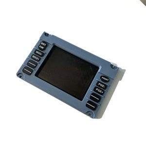 Puede incluir: Un panel de control electrónico gris rectangular con una pantalla central oscura. La unidad tiene botones negros etiquetados como BRT, DIM, MSG-, MSG+, PRINT, PGE- y PGE+, junto con dos botones sin etiqueta a cada lado de la pantalla.