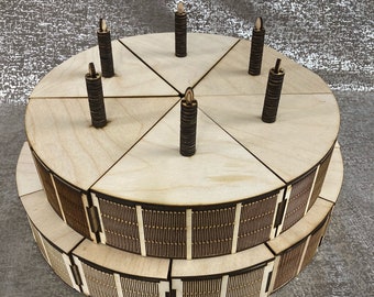 May include: A two-tiered wooden cake with six candles. The cake is made of light wood and has a decorative pattern on the bottom tier. The candles are made of dark wood and have a simple flame design.