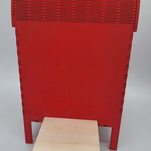 May include: A red wooden mailbox with a hinged top and a small wooden platform with a ring handle. The mailbox is made of wood and has a red paint finish.