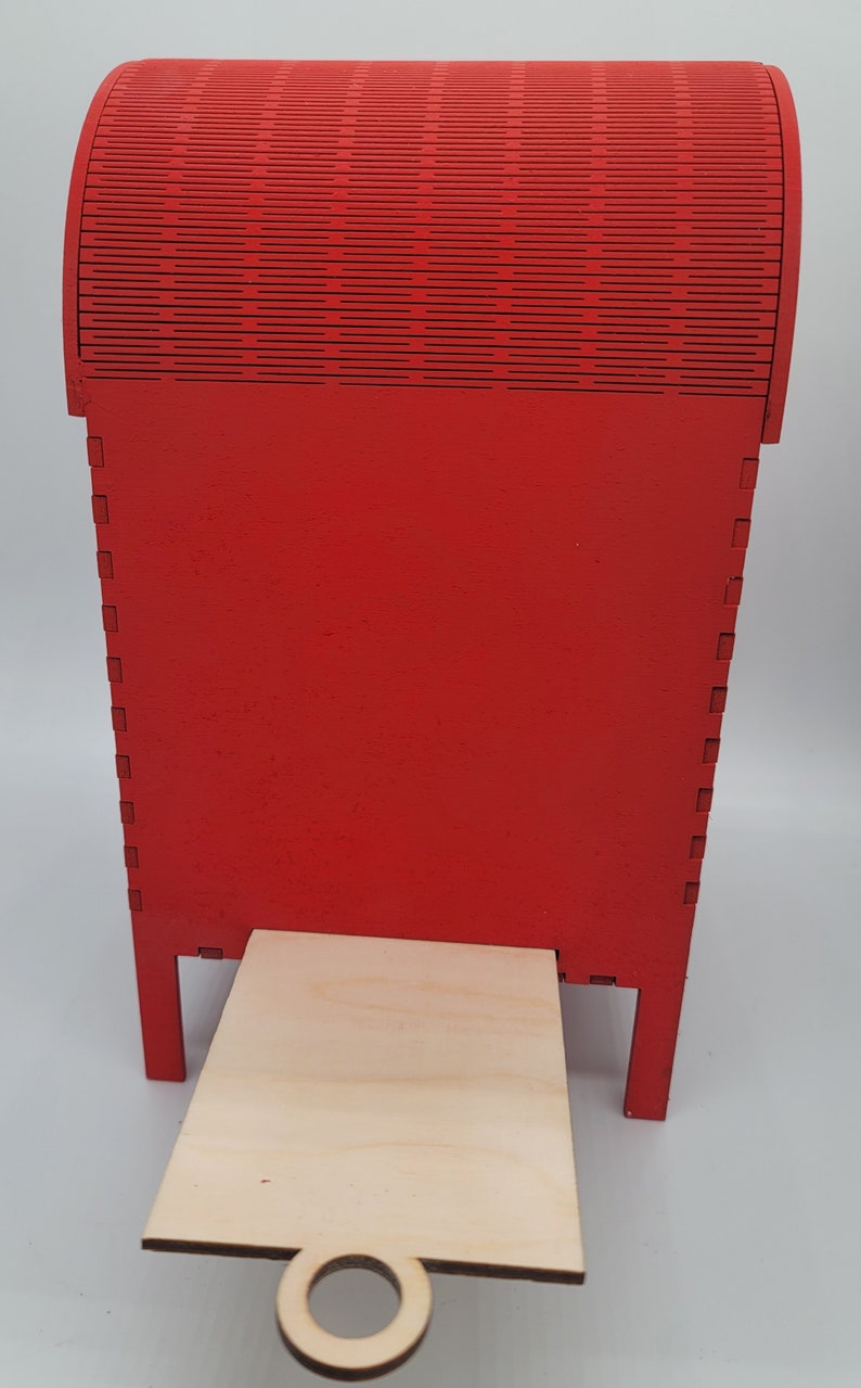 May include: A red wooden mailbox with a hinged top and a small wooden platform with a ring handle. The mailbox is made of wood and has a red paint finish.