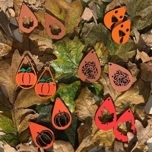 May include: A selection of autumn-themed earrings featuring pumpkins, leaves, and other autumnal designs. The earrings are made of wood and painted in various shades of orange, brown, and red.