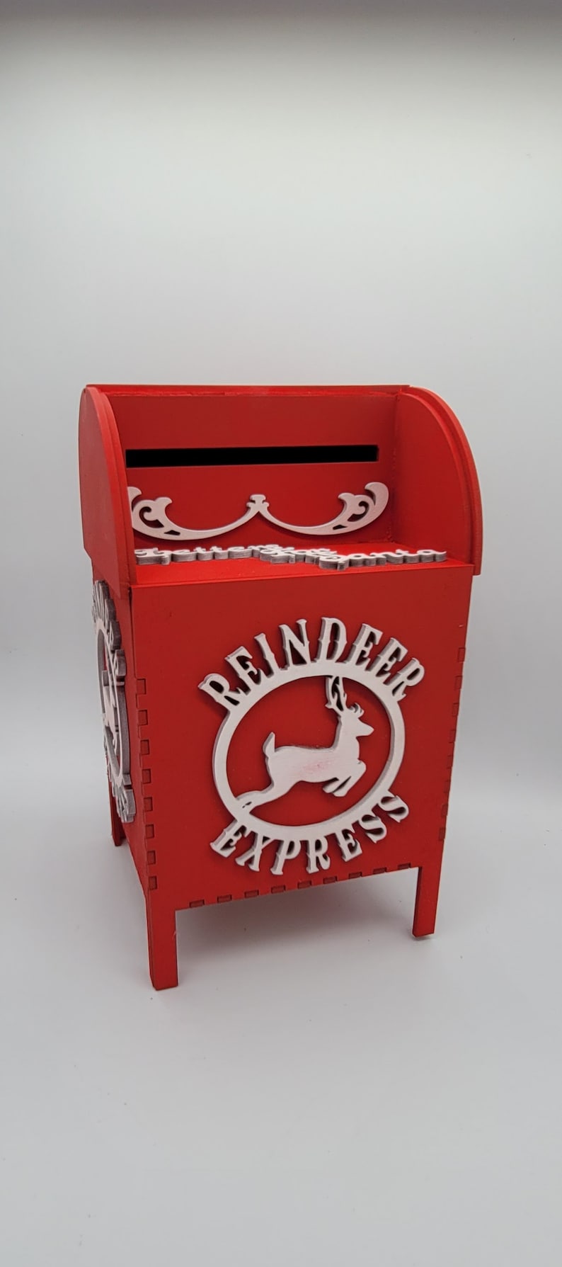 May include: Red wooden mailbox with a white reindeer and "Reindeer Express" text on the front. The mailbox has a slot on the top and stands on four legs.