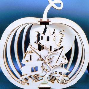 May include: A wooden pumpkin shaped ornament with a laser cut design of a spooky house and a tree. The pumpkin is made of multiple layers of wood and has a hollow center.