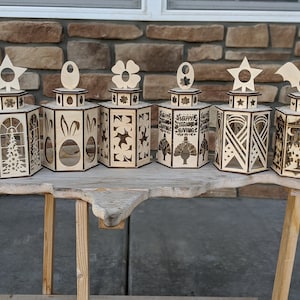 May include: Six wooden candle lanterns with different designs. The lanterns are decorated with stars, flowers, bunnies, a turkey, a ribbon, and a bat. The lanterns are all made of wood and have a natural finish.