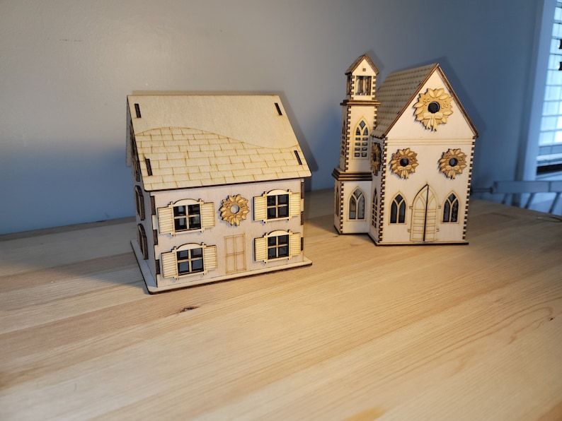 May include: Two wooden Christmas house decorations, one with a traditional design and the other with a more modern design. Both houses have windows and doors, and the modern house has a wreath on the front.