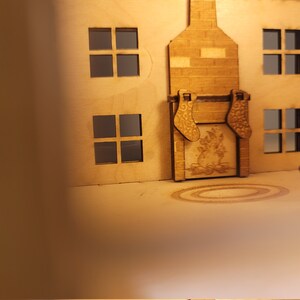 May include: A wooden model of a house with a fireplace and stockings hanging from the mantle. The house has windows and a roof. The fireplace has a fire burning inside.