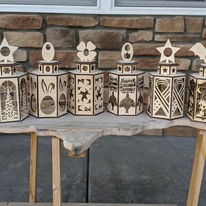 Peut inclure: Six lanternes &agrave; bougies en bois avec des motifs diff&eacute;rents. Les lanternes sont en bois et pr&eacute;sentent une vari&eacute;t&eacute; de motifs d&eacute;coup&eacute;s, notamment des &eacute;toiles, des fleurs, des lapins et une dinde. Les lanternes sont toutes de la m&ecirc;me taille et de la m&ecirc;me forme et sont dispos&eacute;es en rang&eacute;e sur une table en bois.